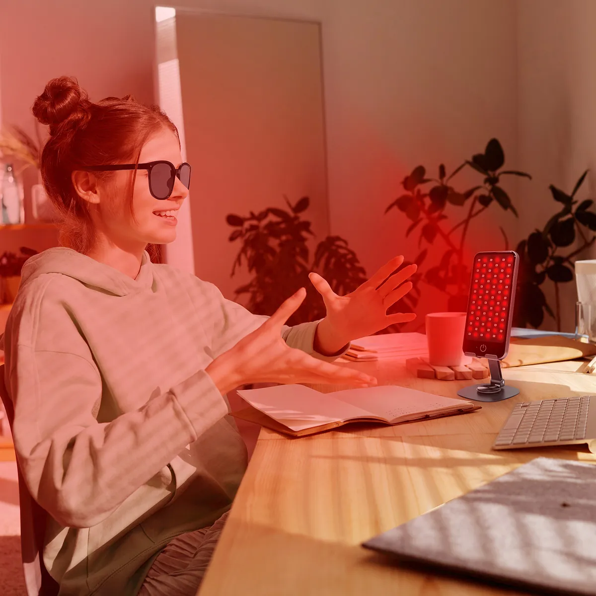 Woman using the Deep Dose red light panel on a desk stand while working